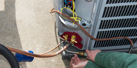 A technician servicing an air conditioner condenser unit