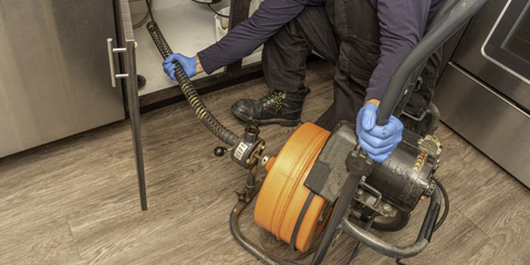 A technician using a drain snake to clear a drain line